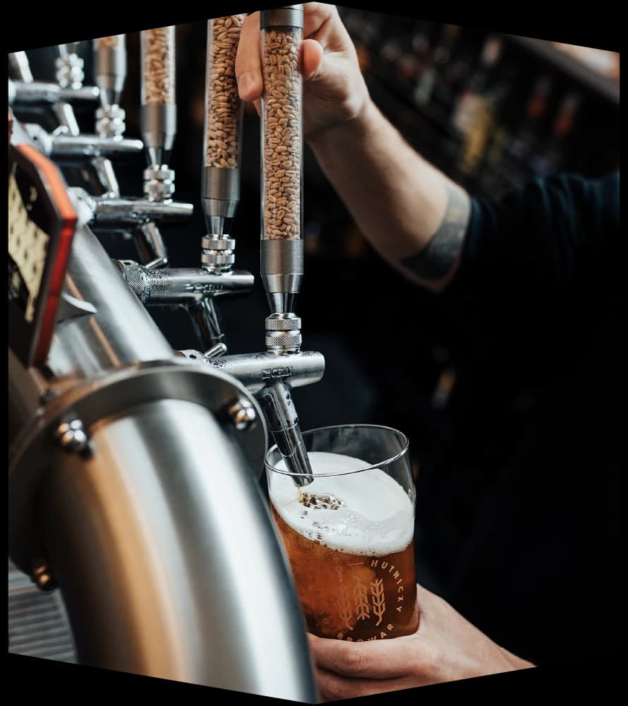 A bartender’s hand on a tap handle filled with malt grain