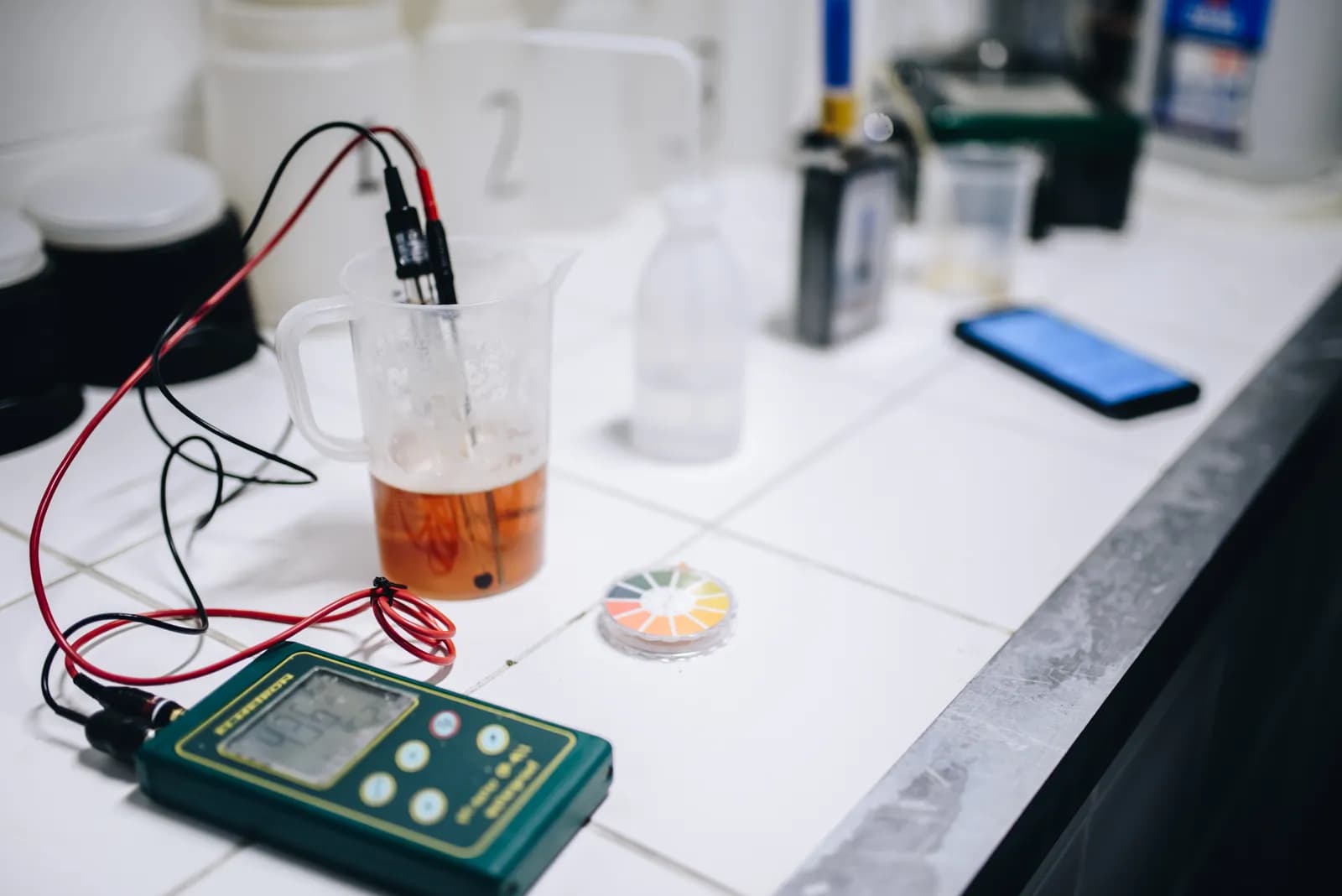 A laboratory meter with probes dipped into a beaker of beer